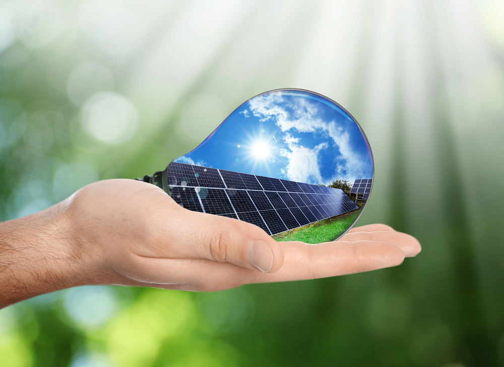 Alternative energy source. Man holding light bulb with solar panels, closeup